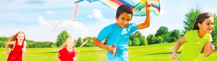 Kids running in a park with a kite.